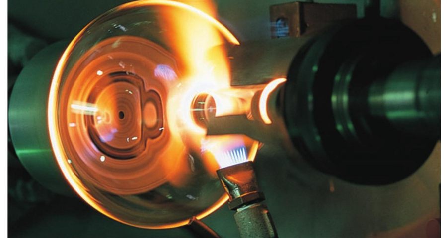 Tube being joined to a vessel on a glass lathe under a burner flame
