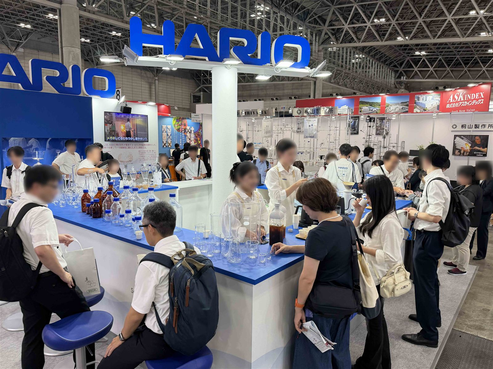 JASIS 2026 ハリオサイエンスのブース。コーヒーカウンターと理化学ガラス製品の前に多くの来場者が集まっている